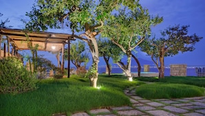 A stone pathway leading to a wooden pergola with a view of a blue building in the background.