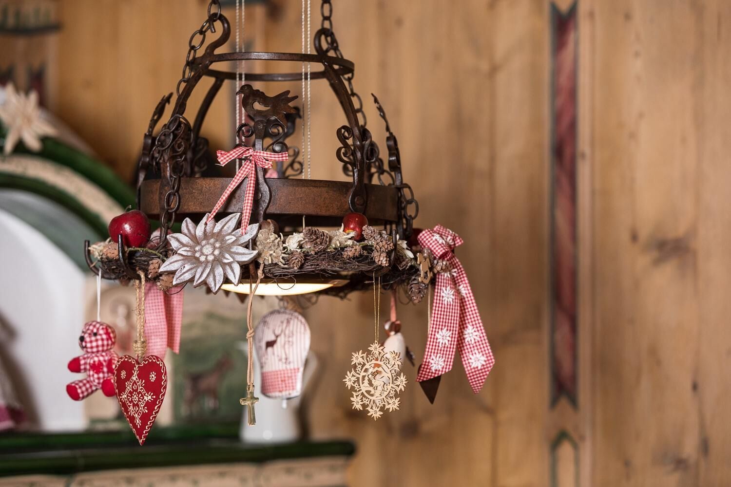 A rustic metal chandelier with various ornaments, including a bird, a flower, and ribbons.