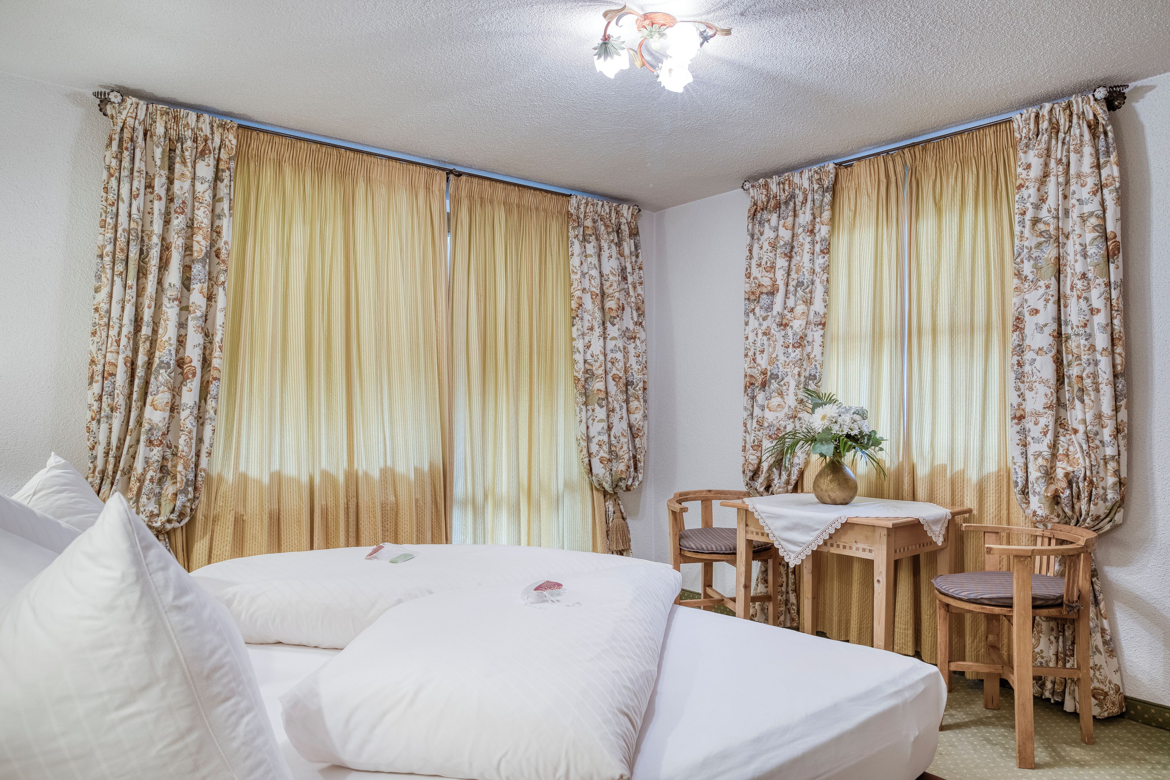 Un dormitorio con una cama, dos sillas, una mesita y cortinas.