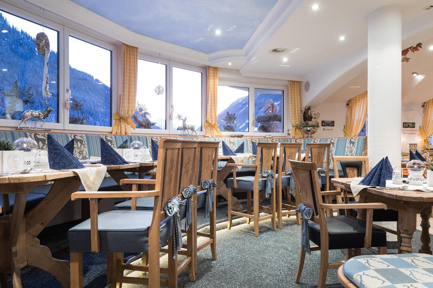 Ein Restaurant mit Holztischen und -stühlen, großen Fenstern mit Blick auf die Berge und einer Decke mit Einbauleuchten.
