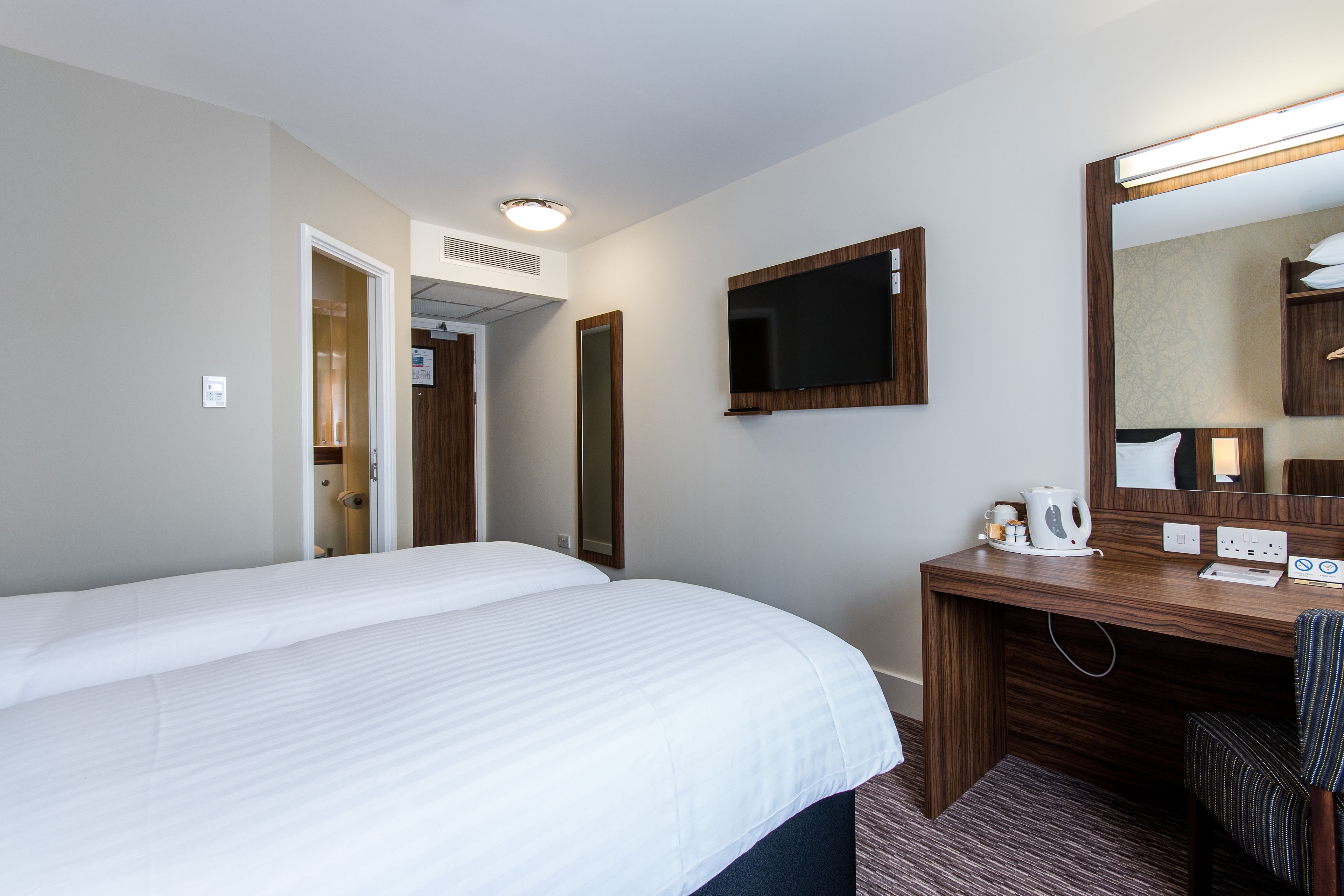 A hotel room with a large bed, a desk with a mirror, a flat-screen TV, and a coffee maker.