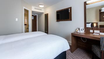 A hotel room with a large bed, a desk with a mirror, a flat-screen TV, and a coffee maker.