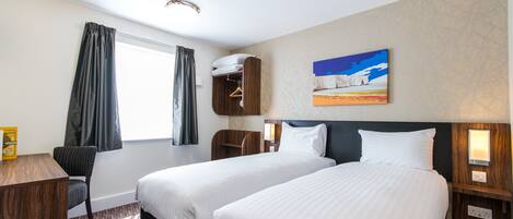 Quarto de hotel com duas camas, uma escrivaninha, uma cadeira, um guarda-roupa e um quadro na parede.