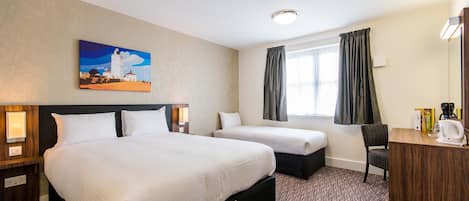 A hotel room with a large bed, a smaller bed, a desk with a chair, a painting on the wall, and a window with curtains.