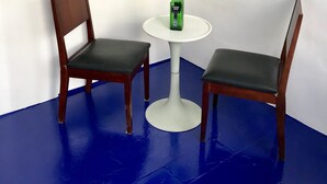 A room with two wooden chairs and a small white table, with a green bottle on the table. - Pousada Axé (Salvador)