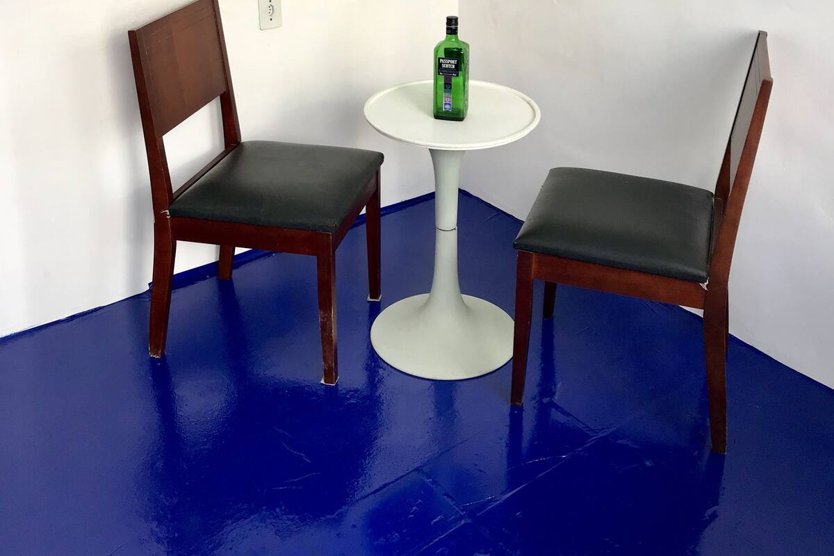 A room with two wooden chairs and a small white table, with a green bottle on the table.