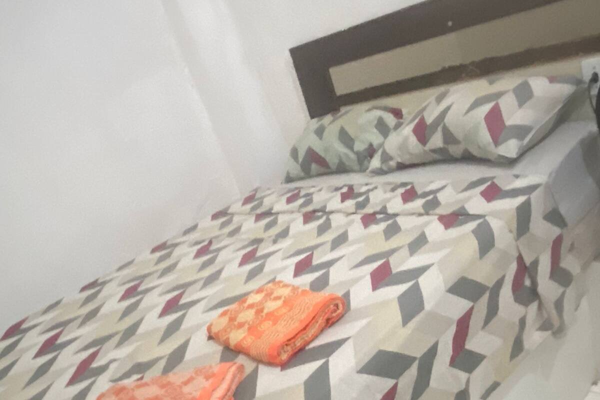 A single bed with a patterned bedspread and two pillows, one with a geometric design and the other with a paisley pattern.