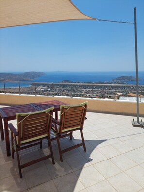 A terrace with a table and chairs, overlooking a coastal landscape with buildings and hills. - Viva B&B (Saronikos)