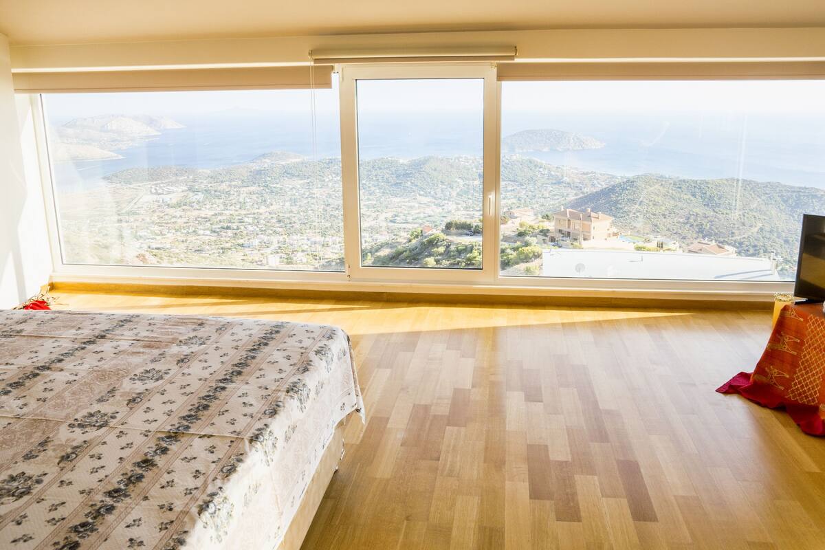 A bedroom with a large window, a bed, a TV, and a small table.