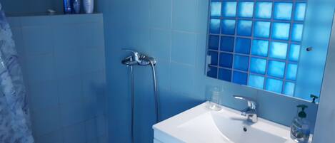 A bathroom with a white sink, a handheld showerhead, and a glass of water on the counter.