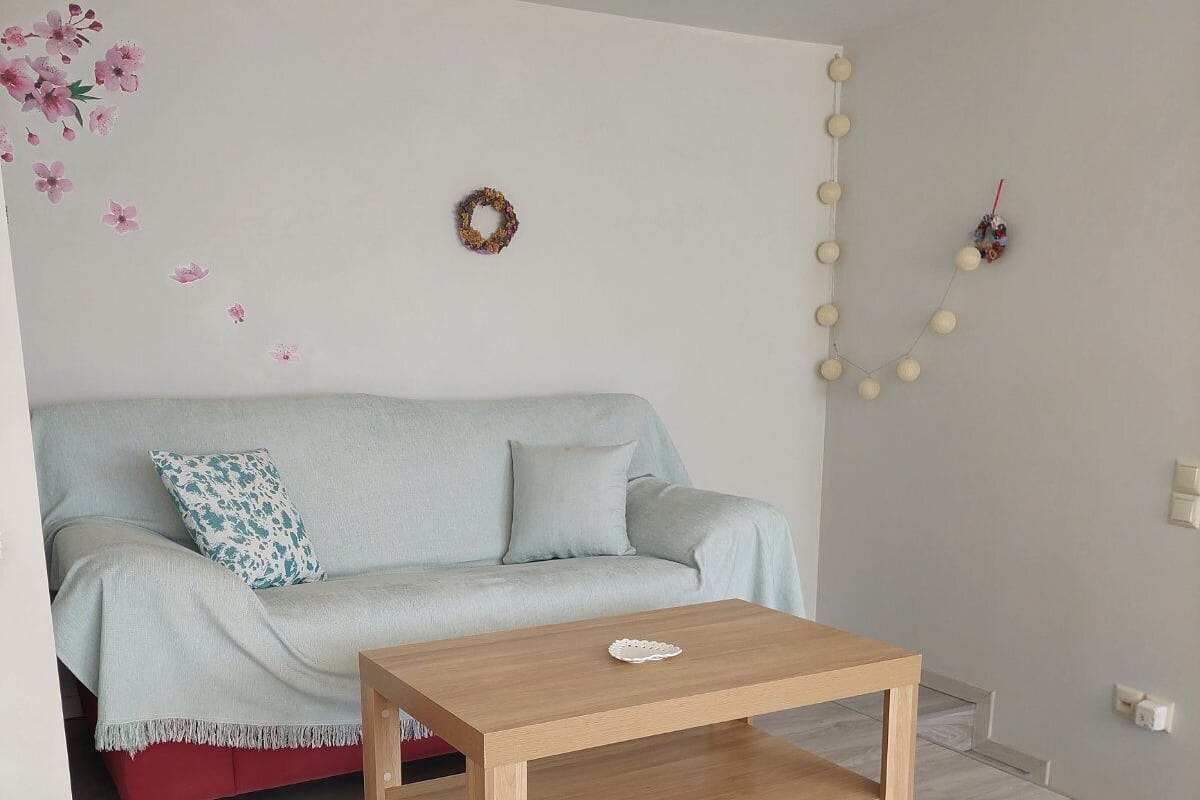 A modern living room with a light blue sofa, a wooden coffee table, and a decorative wall with flowers and a wreath.