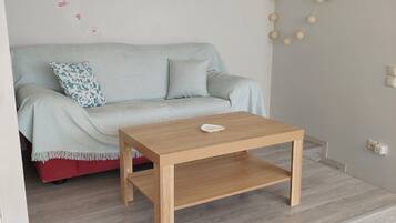 A modern living room with a light blue sofa, a wooden coffee table, and a decorative wall with flowers and a wreath.