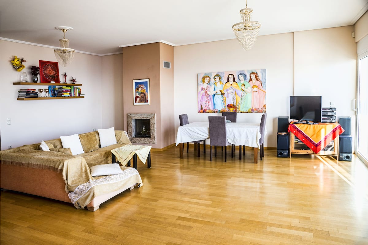 A living room with a sofa, a dining table with chairs, a fireplace, a television, and speakers.