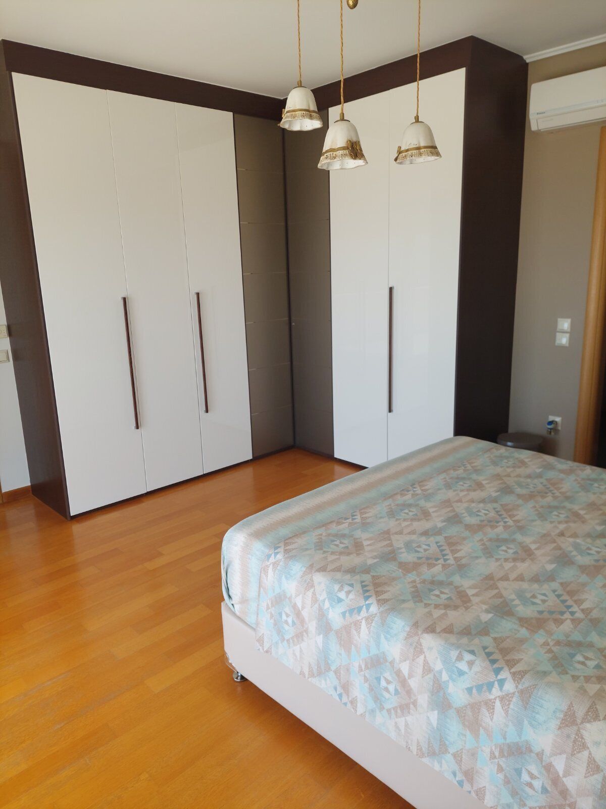 Quarto com cama, soalho de madeira, guarda-roupa e luminárias pendentes.
