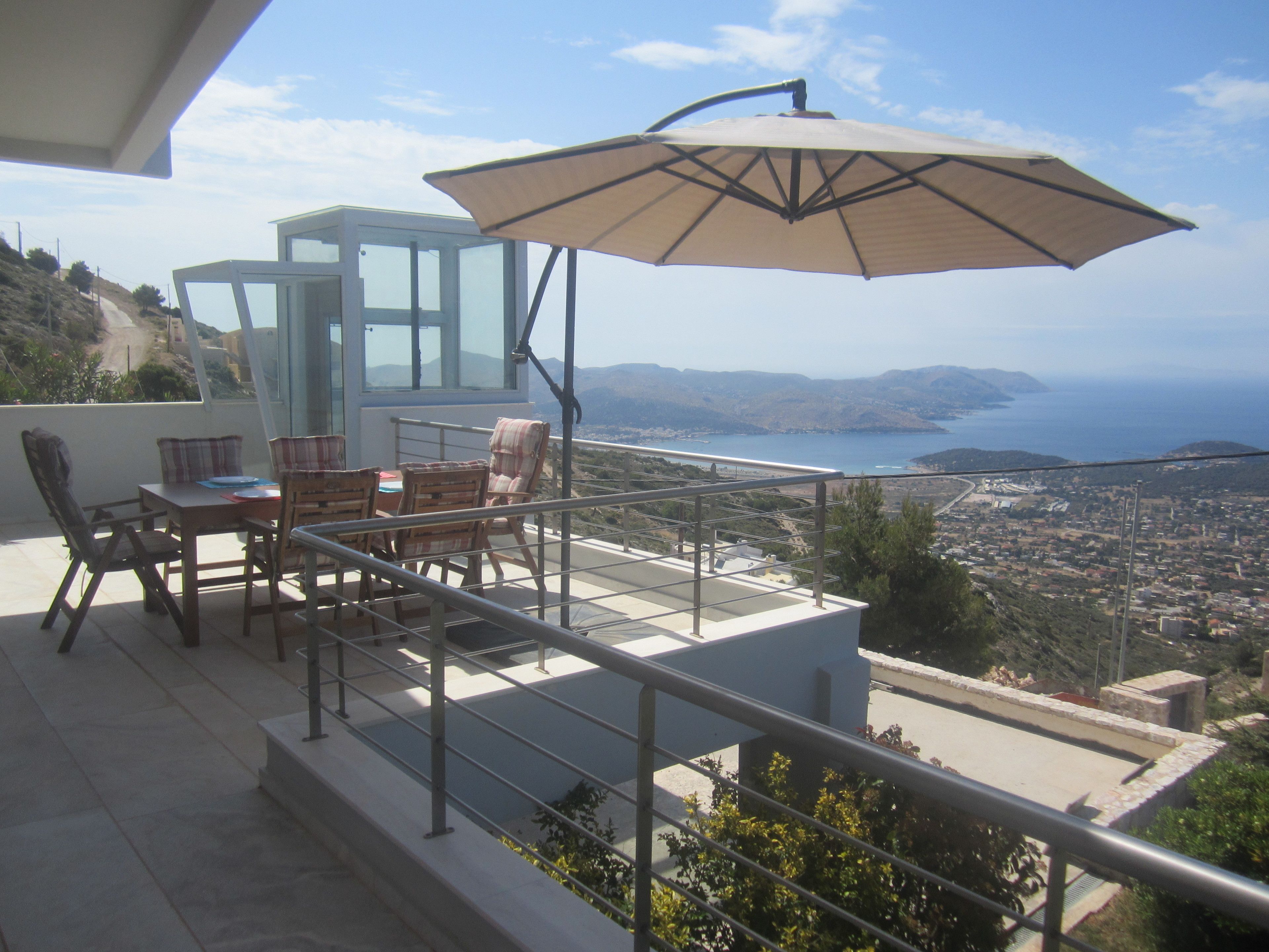 A balcony with a table, chairs, and an umbrella overlooking a coastal cityscape.