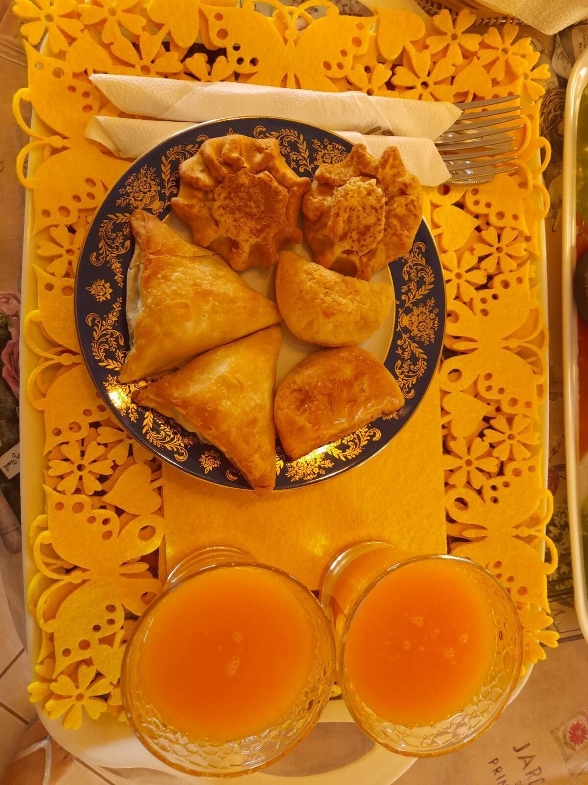 Un plato de samosas y dos vasos de jugo de naranja sobre una mesa con mantel amarillo estampado.