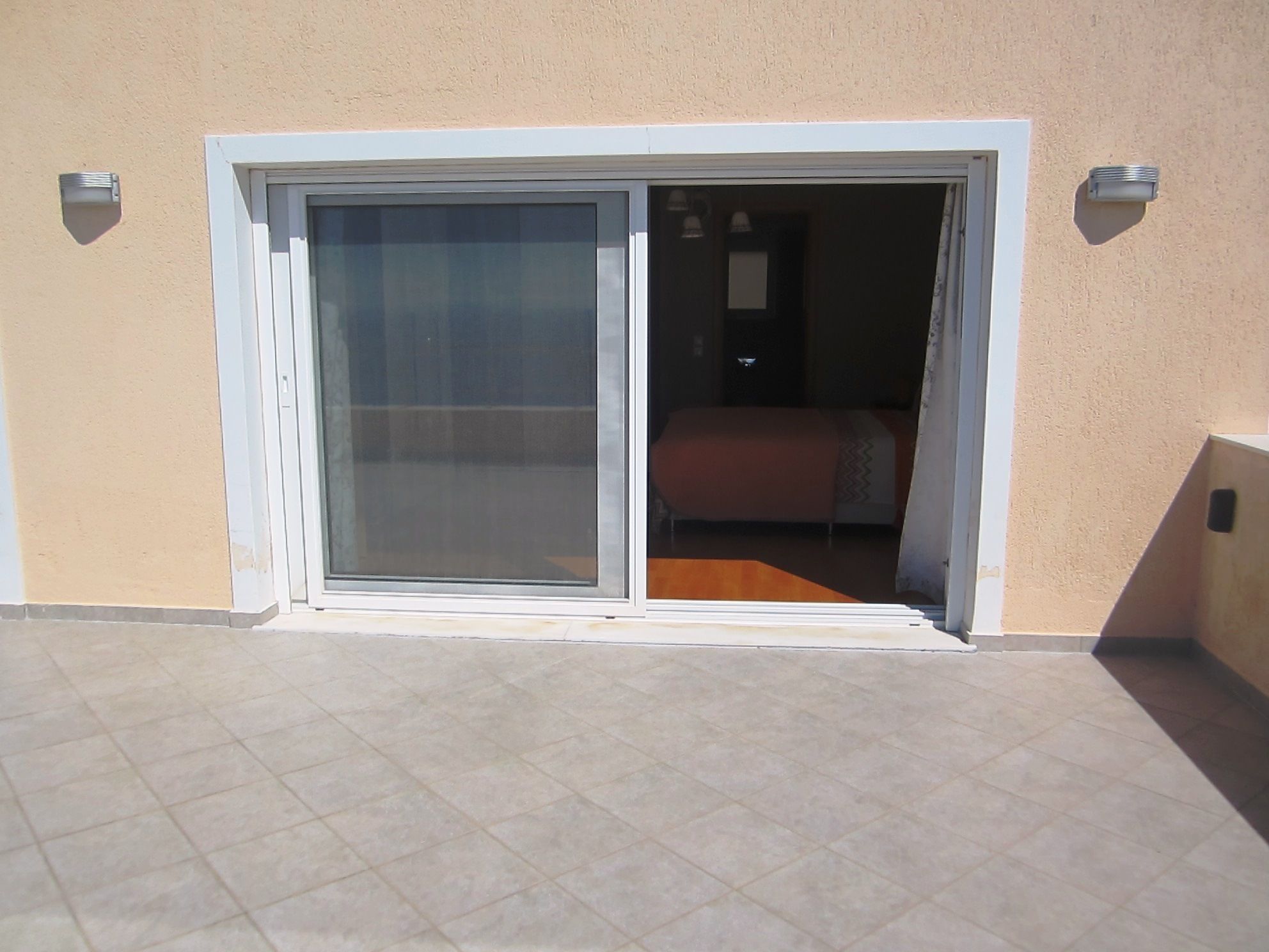 A room with a bed, a window, and a sliding glass door leading to an outdoor area.