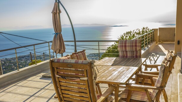 A terrace with a wooden table and chairs, a view of the sea, and a railing. - Viva B&B (Saronikos)