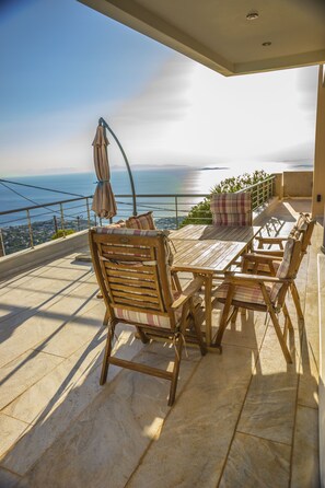 A terrace with a wooden table and chairs, a view of the sea, and a railing. - Viva B&B (Saronikos)