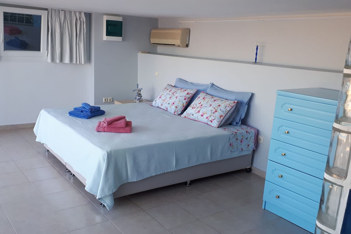 A bedroom with a bed, a blue dresser, a window with curtains, and an air conditioning unit.