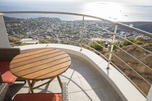 A balcony with a round wooden table and wicker chairs, overlooking a coastal town with buildings and the sea. - Viva B&B (Saronikos)