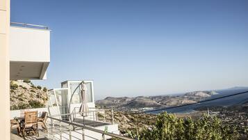 A modern outdoor terrace with a dining area, a glass enclosure, and a scenic view of the coastline and hills.