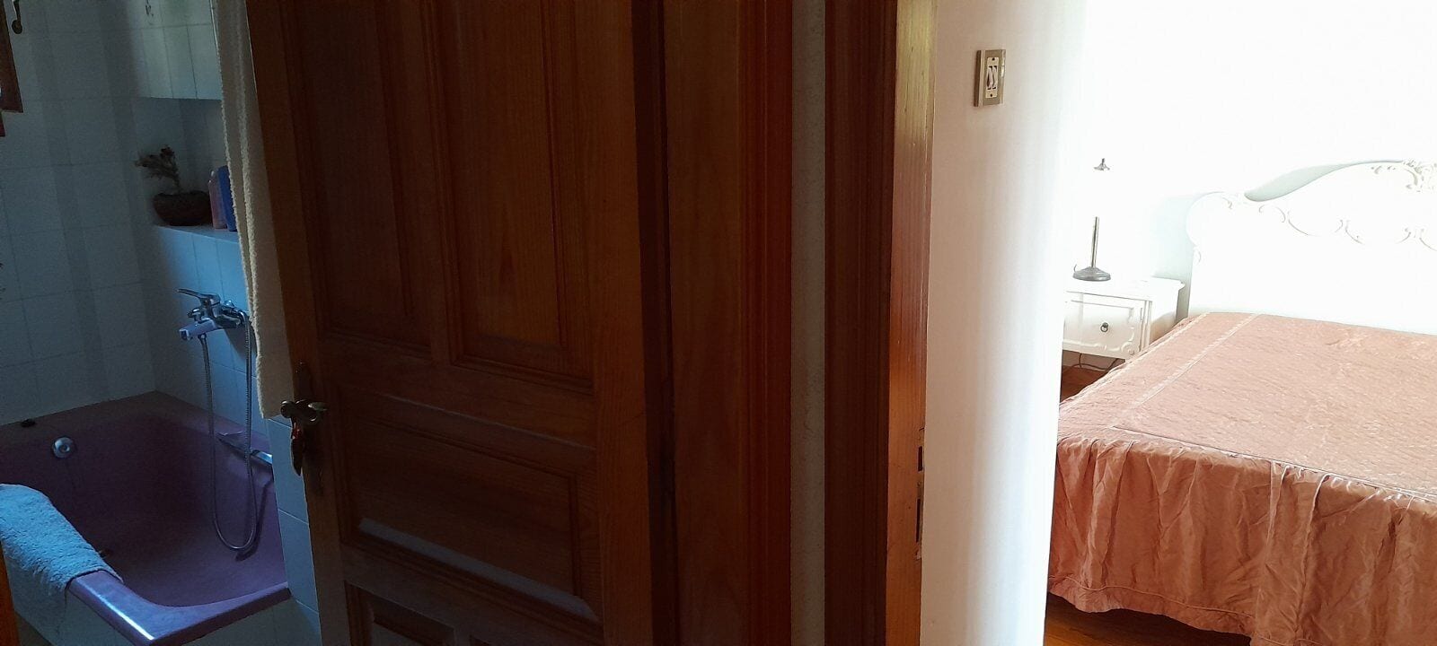 Une salle de bain avec une porte en bois, une baignoire et un lavabo blanc.