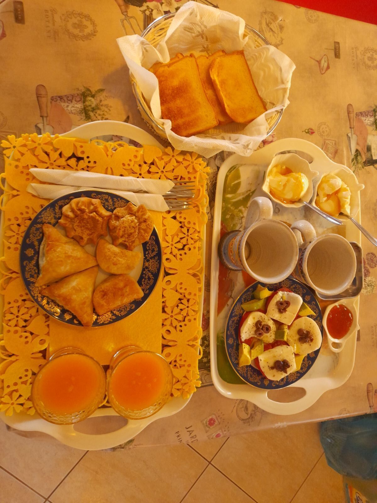 A table set with a variety of dishes including samosas, a plate of sliced vegetables, and two glasses of orange juice.