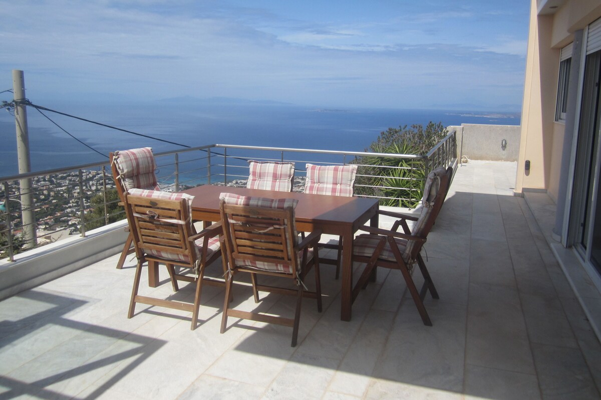 A balcony with a wooden table and chairs, overlooking a coastal view.