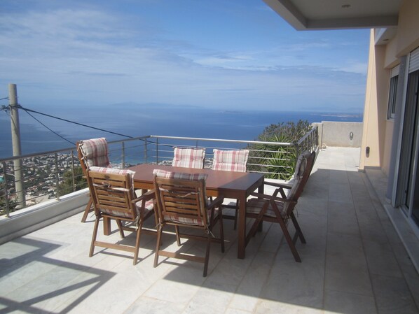 A balcony with a wooden table and chairs, overlooking a coastal view. - Viva B&B (Saronikos)