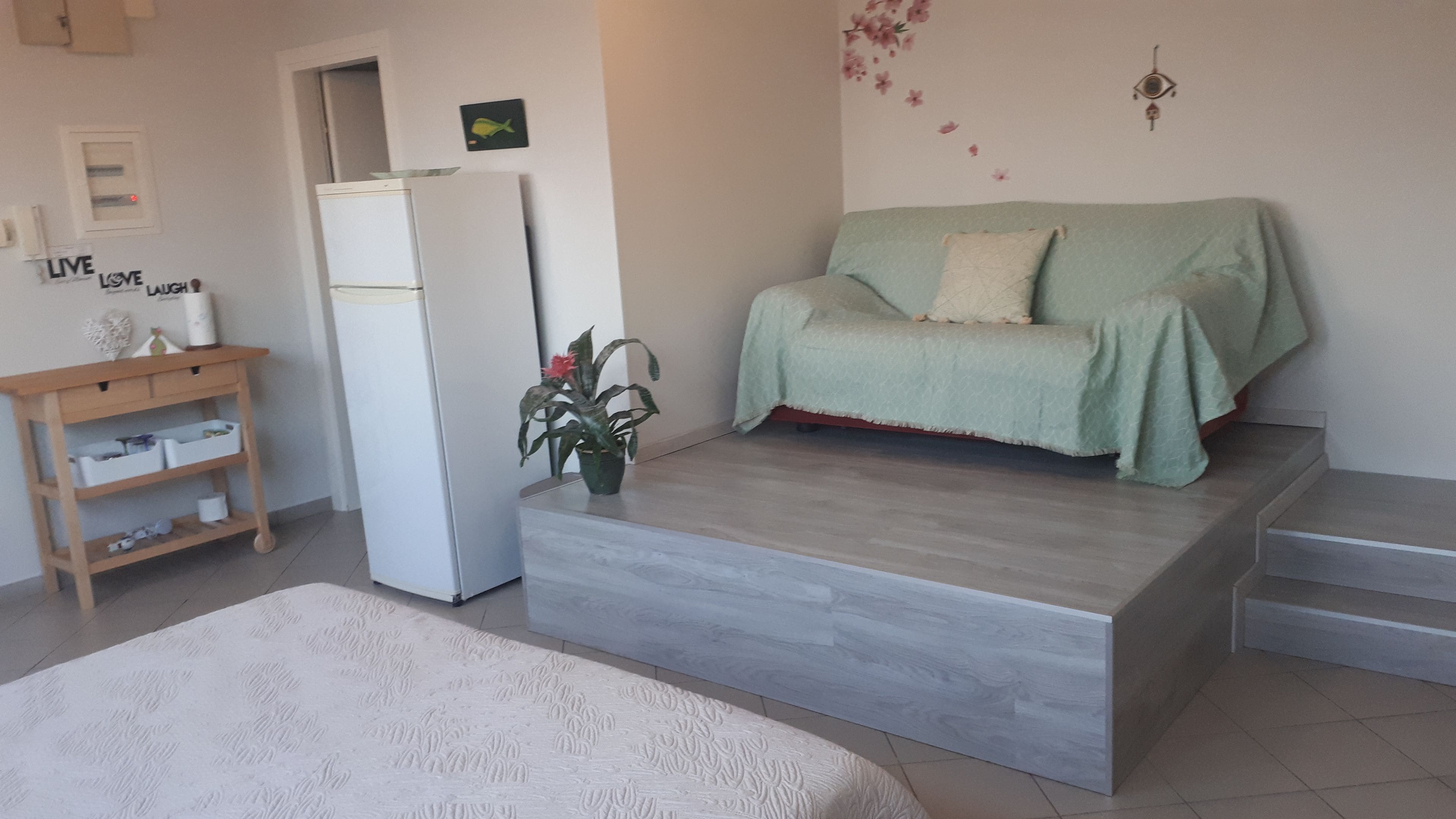 A compact living space with a sofa, a small table, a refrigerator, and a potted plant.
