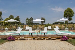 A pool area with lounge chairs and umbrellas, surrounded by greenery and trees. - Villa Marina Velca (Tarquinia)