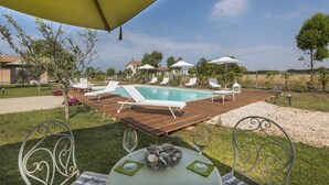 A poolside area with lounge chairs, a wooden deck, and a table with glasses. - Villa Marina Velca (Tarquinia)