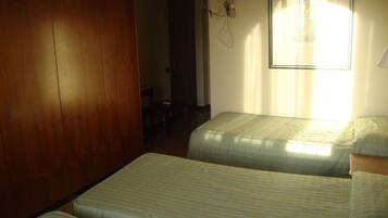 A room with two beds, wooden paneling, a ceiling fan, and a window with curtains.