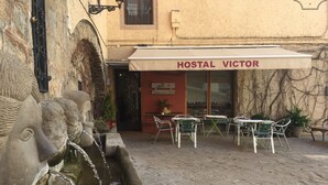 A hostel named 'HOSTAL VICTOR' with outdoor seating and a stone fountain.