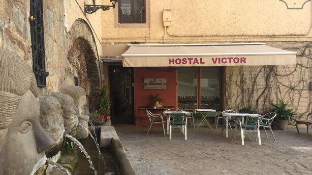 Ein Hostel namens 'HOSTAL VICTOR' mit Außenbestuhlung und einer Steinfontäne.