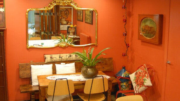 A dining area with a wooden table, chairs, a vase with a plant, a mirror, and a painting on the wall.