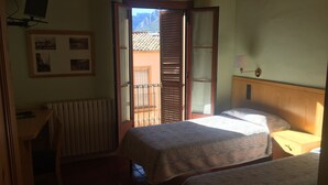 Ein Zimmer mit zwei Betten, einem Schreibtisch, einer Heizung und einem Fenster mit Bergblick.
