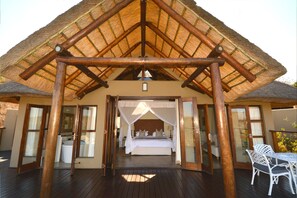 A thatched-roof structure with a wooden frame, a bed with white bedding, and a table with chairs. - Esiweni Luxury Safari Lodge (Ladysmith)