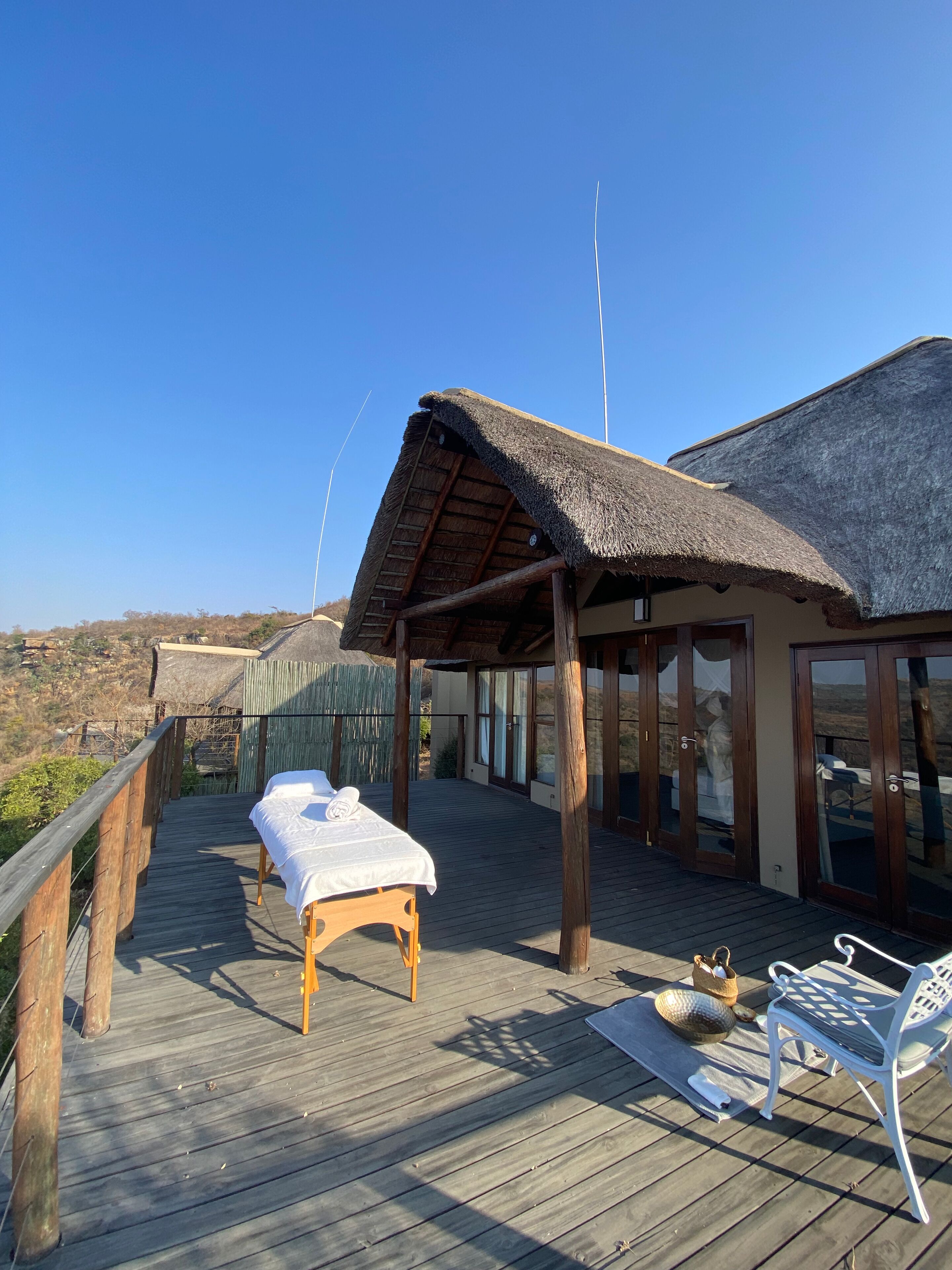 A wooden deck with a bed, a lounge chair, and a thatched-roof structure.
