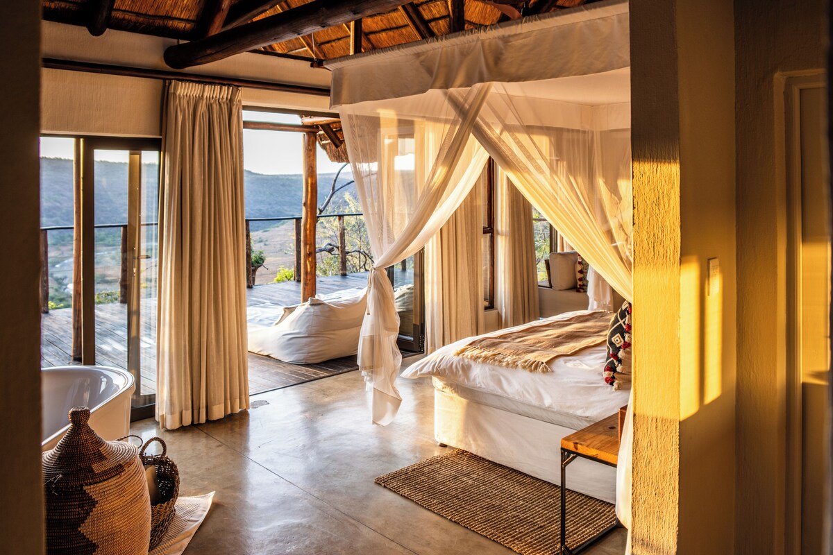 Un dormitorio con cama, mesita de noche, ventana con cortinas y vistas al exterior.