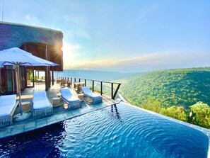 An infinity pool with lounge chairs and umbrellas overlooking a lush landscape. - Esiweni Luxury Safari Lodge (Ladysmith)