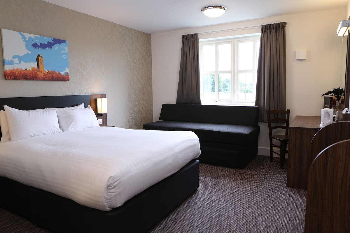A hotel room with a large bed, a sofa, a desk, and a window with curtains.