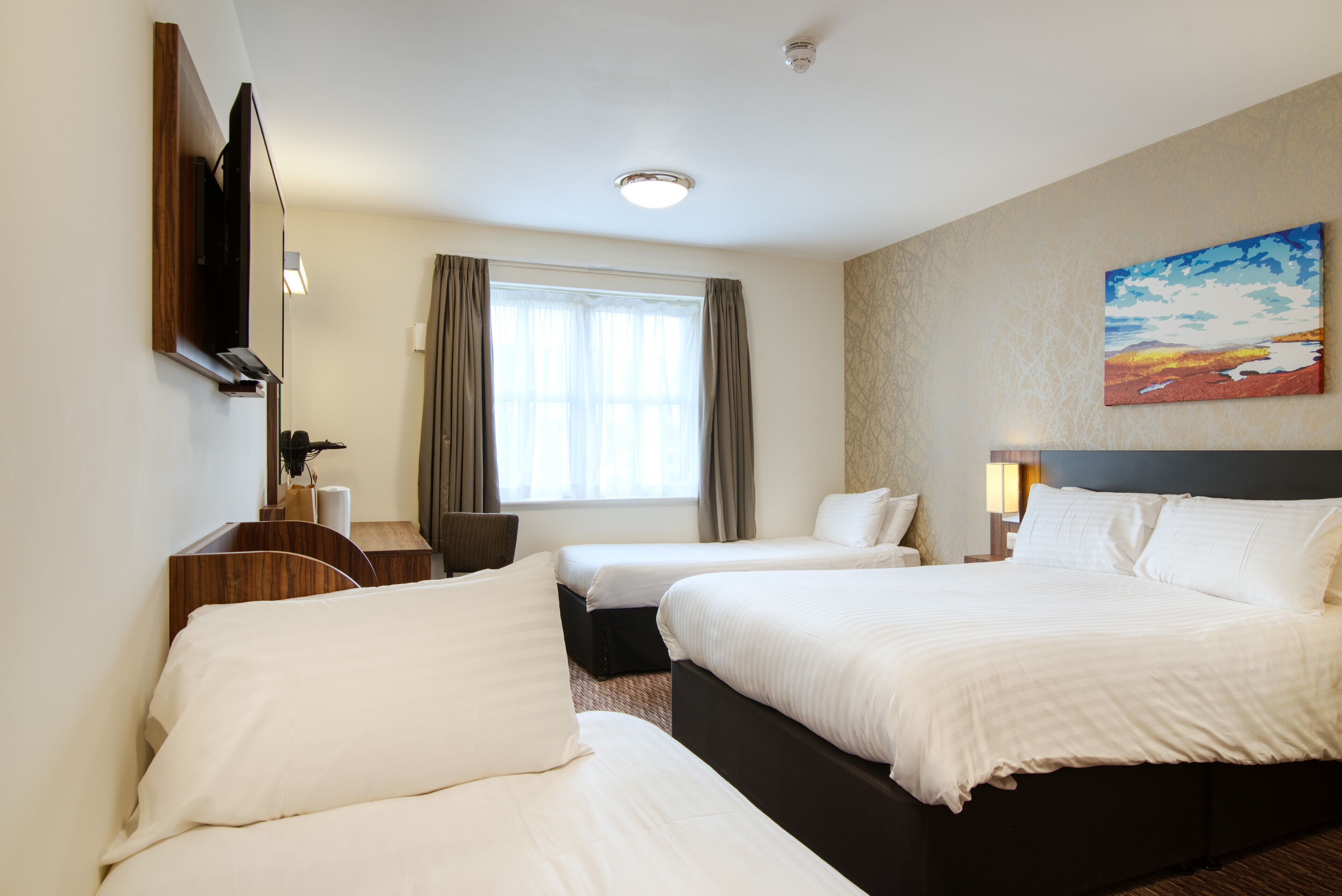 Habitación de hotel con dos camas, un escritorio, una silla y un cuadro en la pared.