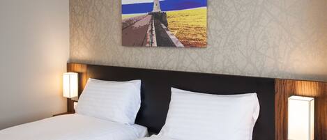 Une chambre d’hôtel avec un lit, deux lampes de chevet et un tableau représentant un phare, accroché au mur.