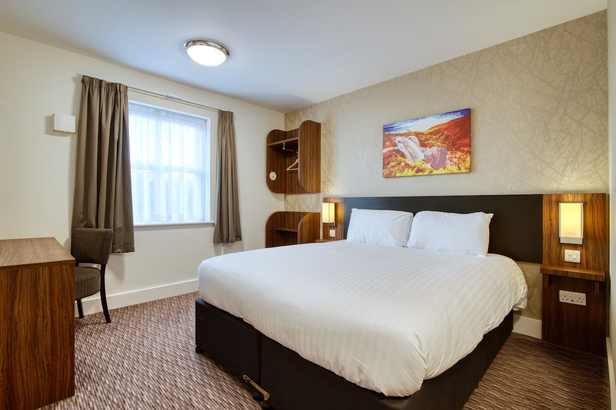 A hotel room with a large bed, a desk, a chair, a wardrobe, and a painting on the wall.