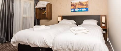 Quarto de hotel com duas camas, cabeceira de madeira, um quadro na parede e uma janela com cortinas.