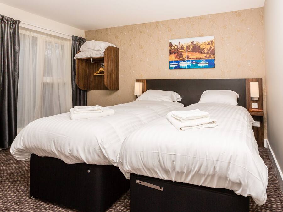 Een hotelkamer met twee bedden, een houten hoofdeinde, een schilderij aan de muur en een raam met gordijnen.