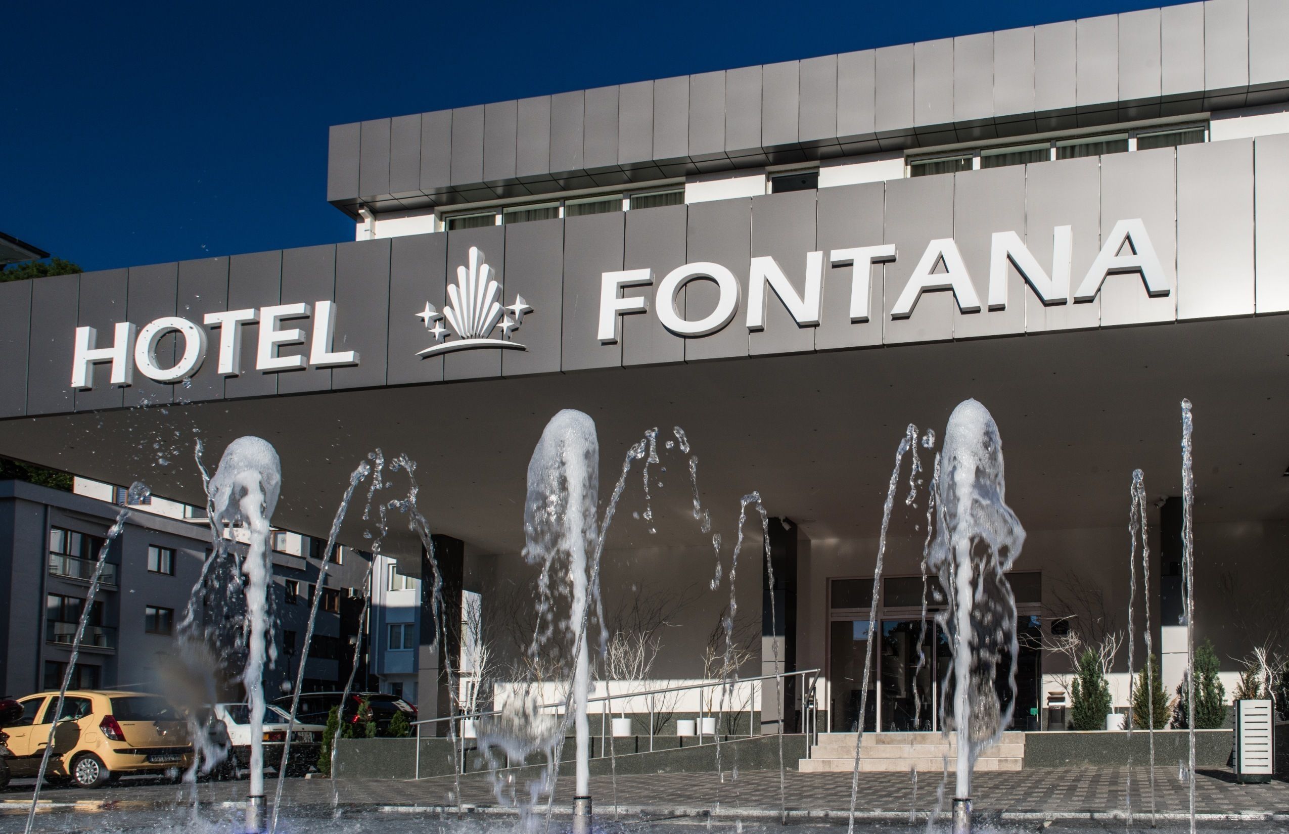 Un hotel llamado Fontana con una fachada moderna y una fuente de agua en primer plano.