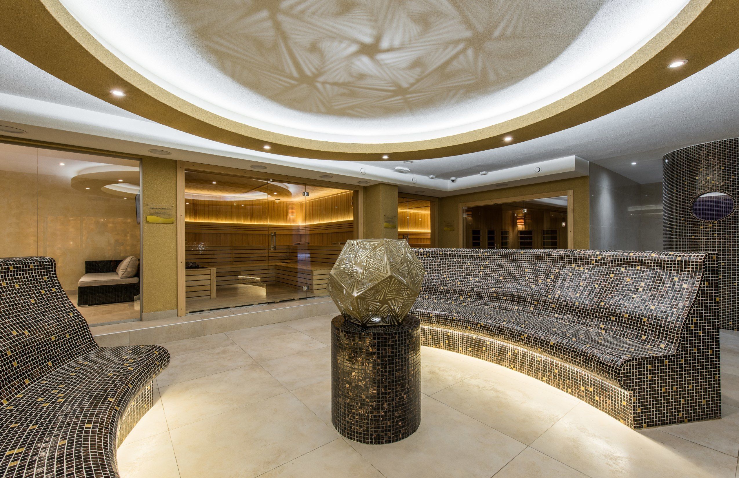 A modern lobby with a curved ceiling, a mosaic bench, and a central decorative sculpture.